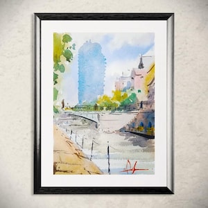 Op de afbeelding: Aquarel schilderij van een stadsgezicht met een rivier en brug. Het kunstwerk toont een hoog blauw gebouw, een brug en gebouwen met roze en gele tinten. De schildering is ingelijst in een zwarte lijst.