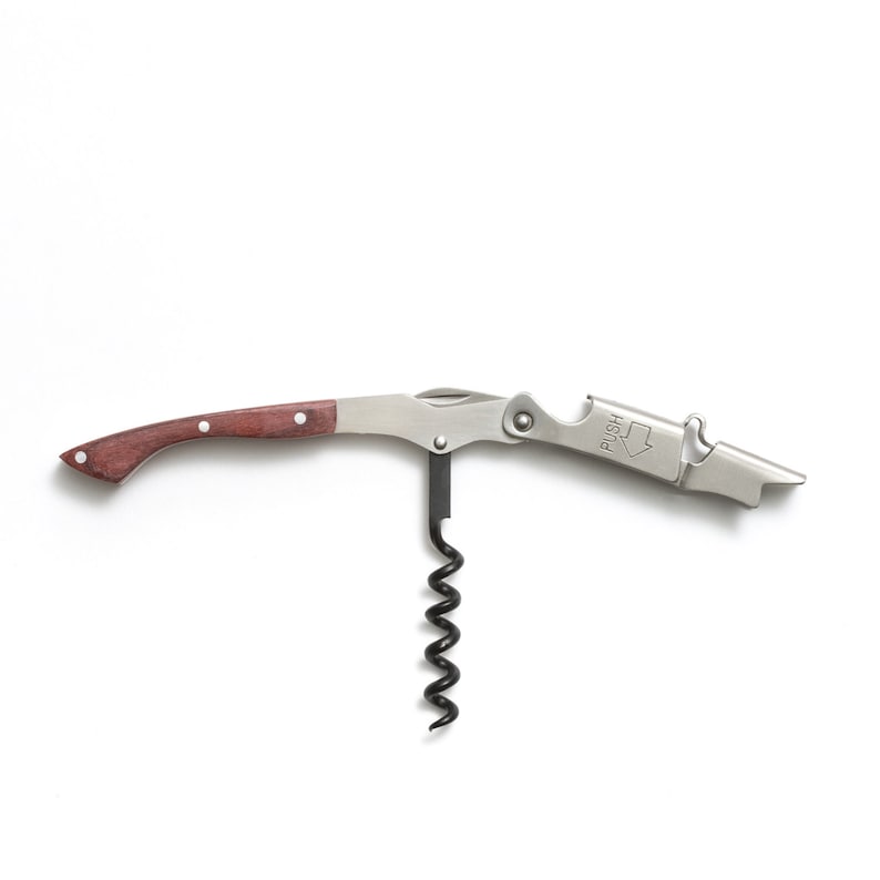 May include: A silver wine opener with a wooden handle and a corkscrew. The opener has a built-in bottle opener and a lever to help remove the cork. The opener has the word "PUSH" printed on it.