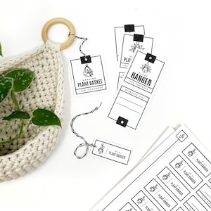 May include: A cream-colored, crocheted hanging plant basket with a wooden ring and a black and white string. Several white tags with black text that reads "HANGING PLANT BASKET" and "MINI PLANT HANGER" are scattered around the basket.