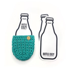 May include: A teal blue crocheted bottle cozy with a small wooden button. The cozy is displayed on a white card with a black outline of a bottle and the text "Bottle Cozy 100% Handmade".