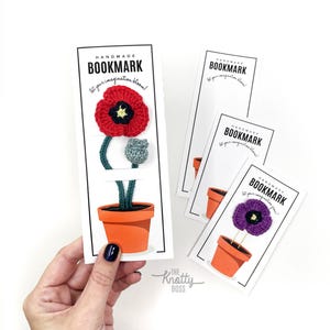 Peut inclure: Marque-page fait à la main avec une fleur rouge crochetée, une tige verte et un bouton gris dans un pot orange. Le marque-page porte l'inscription "BOOKMARK" et "Let your imagination bloom!"