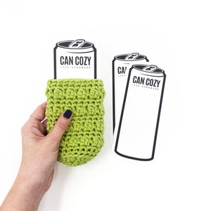 May include: Two white stickers with black text and illustrations of a can with the text "CAN COZY 100% HANDMADE" on them. A green crocheted can cozy is being held in a hand.