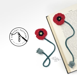 Puede incluir: Marcadores de ganchillo de amapolas en rojo, verde y gris. Los marcadores presentan una flor de amapola roja con un centro negro y detalles verdes, conectada a un tallo verde. También se ve el logotipo "The Knotty Boss".