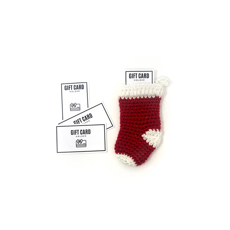 May include: Four white gift card holders with the text "Gift Card Holder" and a small gift box icon. The holders are next to a small red and white crocheted stocking.