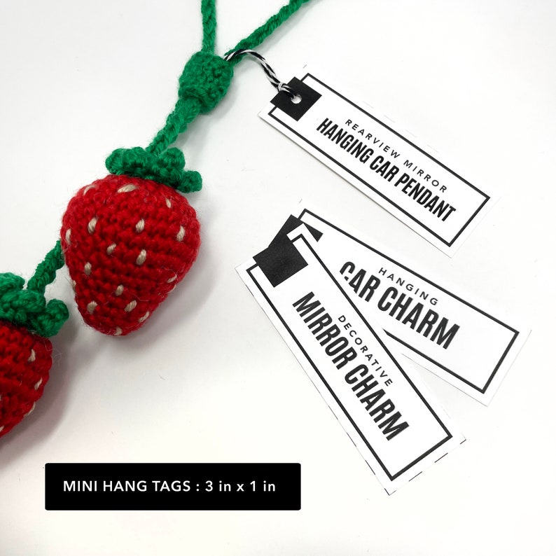 May include: Two crocheted strawberry charms with green stems and leaves hanging from a green cord. The charms are attached to two white hang tags with black text. The top tag reads "Rearview Mirror Hanging Car Pendant". The bottom tag reads "Hanging Car Charm Decorative Mirror Charm". The text at the bottom of the image reads "Mini Hang Tags: 3 in x 1 in".