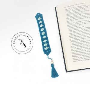 Op de afbeelding: Teal gehaakte bladwijzer met een bloemenontwerp en een kwast. De bladwijzer heeft lichtblauwe bloemaccenten en een bijpassende kwast met houten kralen. Het logo "CROCHET PATTERN THE KNOTTY BOSS" is ook zichtbaar.