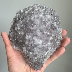 May include: A cluster of translucent, light gray quartz crystals with a jagged, multi-faceted surface. The mineral formation features numerous small, pointed crystal points that catch the light, displaying a mix of clear and smoky gray tones.