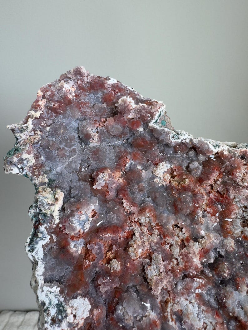 Op de afbeelding: Een groot mineraalexemplaar met een cluster van kristallijne formaties in tinten van diep roodbruin, doorschijnend grijs en wit. Het oppervlak is getextureerd met kleine, grillige kristalpunten en ruwe, onregelmatige randen overal.