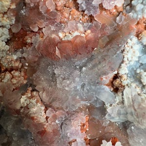 Op de afbeelding: Een mineraalexemplaar met een cluster van doorschijnende, lichtroze tot heldere kwartskristallen, afgewisseld met levendige oranjerode ijzeroxide-insluitingen. De formatie toont een mix van scherpe, puntige kristallen en korrelige texturen.