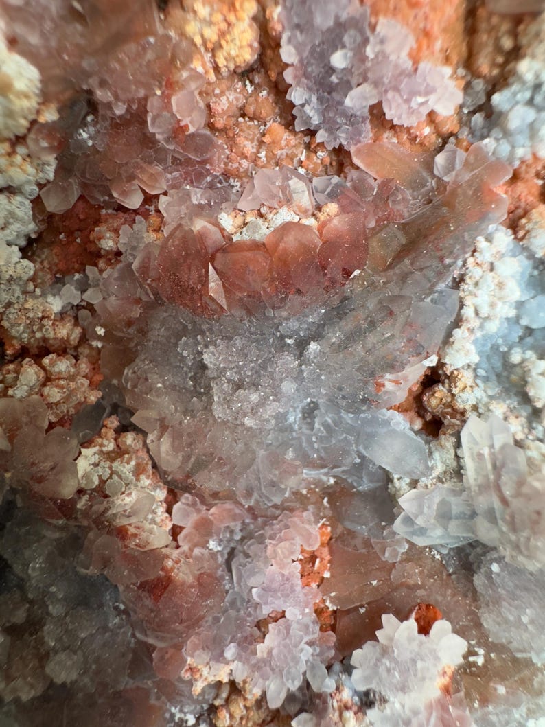 Op de afbeelding: Een mineraalexemplaar met een cluster van doorschijnende, lichtroze tot heldere kwartskristallen, afgewisseld met levendige oranjerode ijzeroxide-insluitingen. De formatie toont een mix van scherpe, puntige kristallen en korrelige texturen.