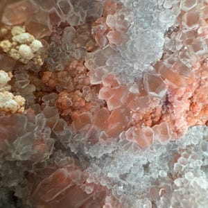 Op de afbeelding: Een mineraalexemplaar met een cluster van doorschijnende, zeshoekige kwartskristallen afgewisseld met getextureerde, zalmroze mineraalformaties. De kristalstructuur vertoont heldere punten van verschillende groottes en dichte, korrelige afzettingen.
