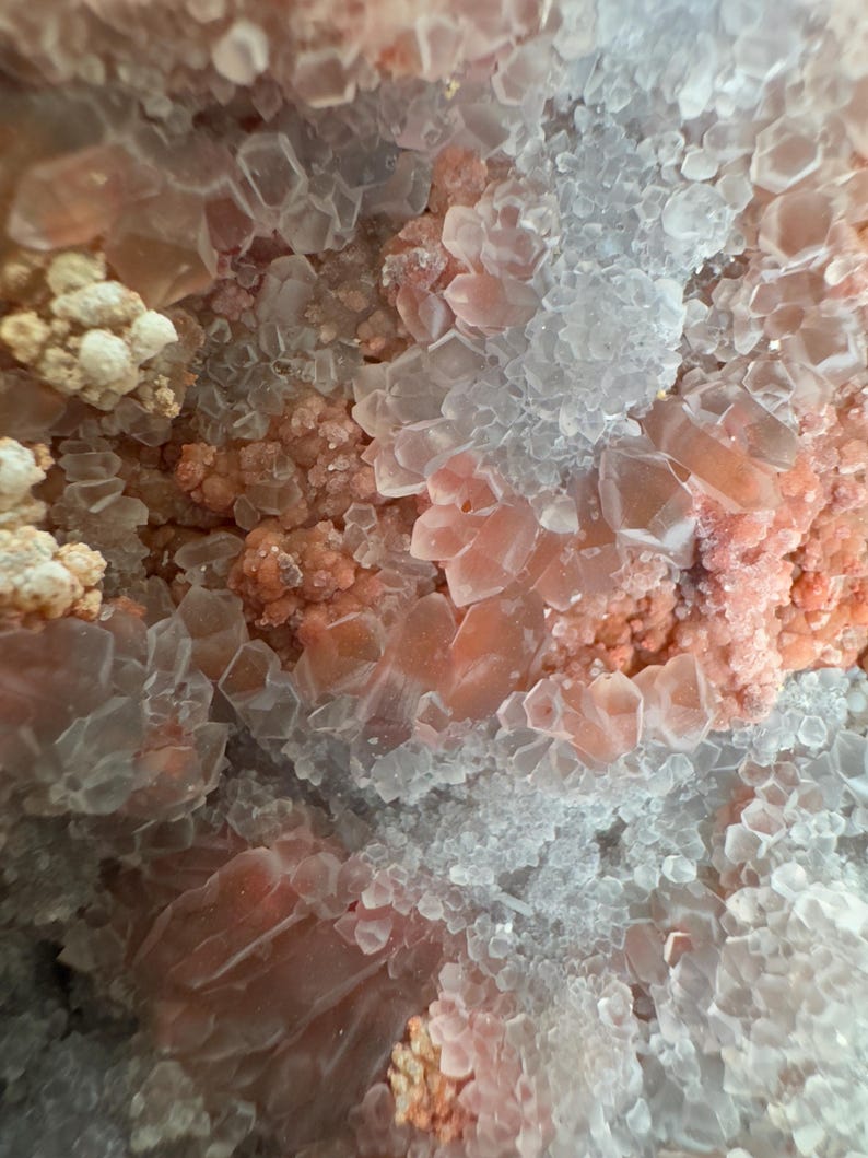 Op de afbeelding: Een mineraalexemplaar met een cluster van doorschijnende, zeshoekige kwartskristallen afgewisseld met getextureerde, zalmroze mineraalformaties. De kristalstructuur vertoont heldere punten van verschillende groottes en dichte, korrelige afzettingen.