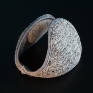 May include: Gray earmuffs with a soft, textured exterior and a plush interior. The earmuffs have a simple, rounded design with a gray trim. The ear covering is designed to keep ears warm in cold weather.