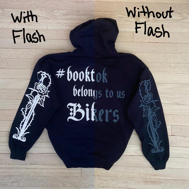 May include: A navy blue hoodie with the text "#booktok belongs to us Bikers" on the back. The sleeves feature a rose and dagger design. The image is shown with and without flash.