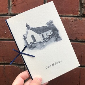 May include: A folded card featuring a watercolour illustration of a church and graveyard, tied with a navy blue ribbon. The words "Order of Service" are printed on the card.