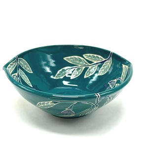 May include: A white ceramic mug with a black handle and the text "But First, Coffee" in a bold, black font. The mug is set against a blurred background, suggesting a cozy setting.