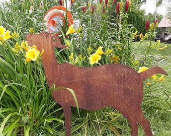 May include: A rusty metal silhouette of a goat standing in a garden with yellow flowers and green foliage.