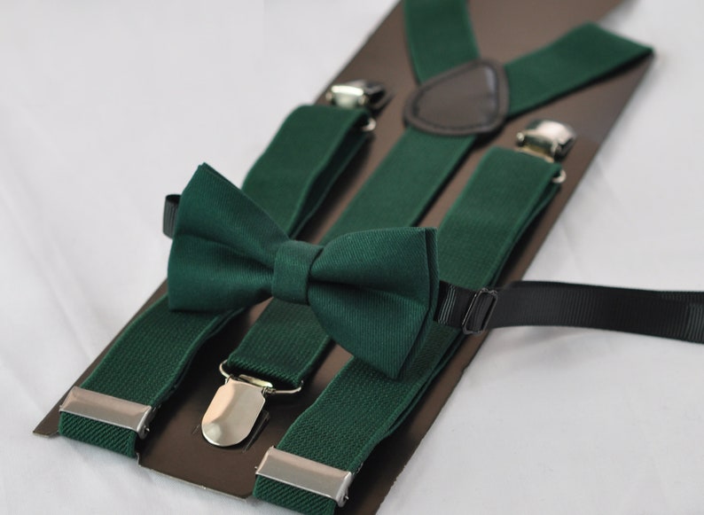 May include: A set consisting of a dark forest green bow tie and matching elastic braces. The braces feature silver-toned metal clips and a dark brown leather-like back patch. The bow tie is pre-tied and includes a black adjustable strap.