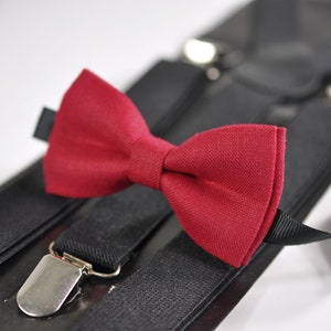 Puede incluir: Un juego de tirantes negros con una pajarita roja. Los tirantes tienen clips plateados y la pajarita está hecha de una tela texturizada.