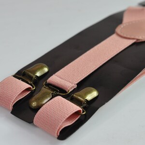 Peut inclure: Une paire de bretelles roses avec des clips en m&eacute;tal dor&eacute; antique. Les bretelles sont faites d'un tissu doux et tiss&eacute; et sont r&eacute;glables.