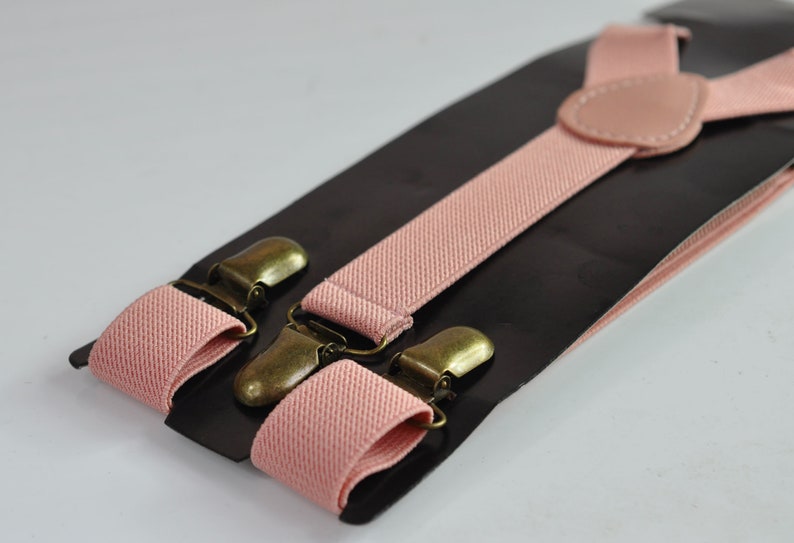 Peut inclure: Une paire de bretelles roses avec des clips en m&eacute;tal dor&eacute; antique. Les bretelles sont faites d'un tissu doux et tiss&eacute; et sont r&eacute;glables.