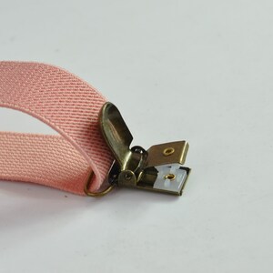 Peut inclure: Une sangle &eacute;lastique rose avec un clip en m&eacute;tal dor&eacute;. Le clip a un insert en plastique blanc avec deux petits trous.