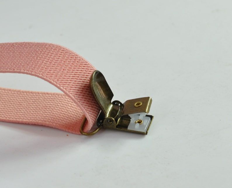 Peut inclure: Une sangle &eacute;lastique rose avec un clip en m&eacute;tal dor&eacute;. Le clip a un insert en plastique blanc avec deux petits trous.