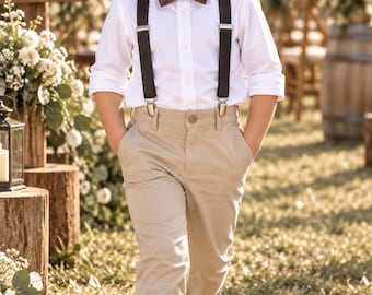 May include: A white long-sleeved button-down shirt, dark brown bow tie, dark brown suspenders with silver clips, and khaki trousers. The outfit is completed with dark brown leather shoes, creating a formal ensemble for a ring bearer.