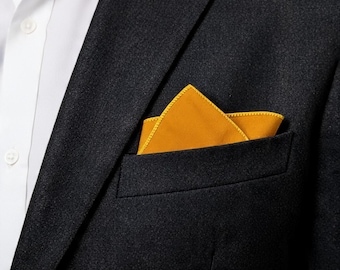 May include: A dark charcoal gray blazer with a crisp white collared shirt underneath. A vibrant mustard yellow pocket square is neatly folded and tucked into the breast pocket of the blazer, featuring a visible stitched edge detail.
