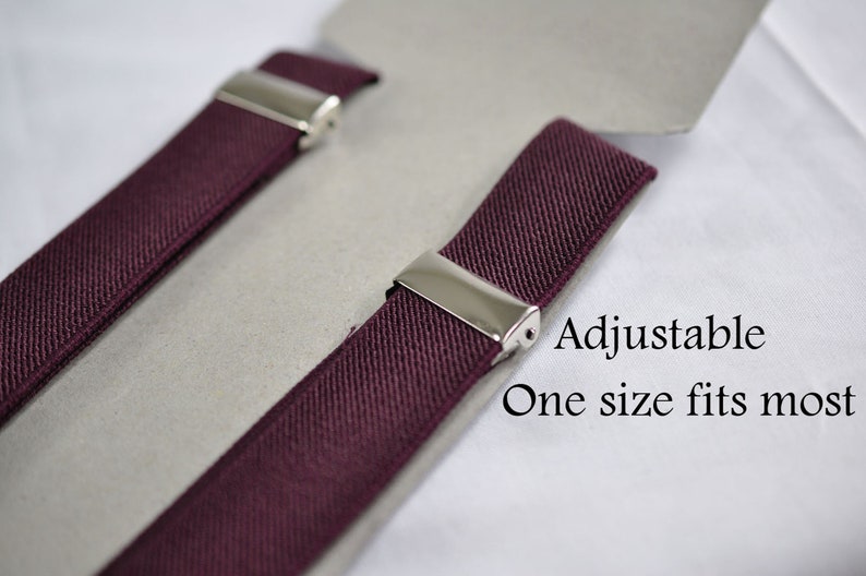 May include: A pair of burgundy elastic suspenders featuring polished silver-tone metal clips for adjustment. The product is displayed on a light gray card with the printed text: Adjustable, One size fits most. The fabric has a woven texture.