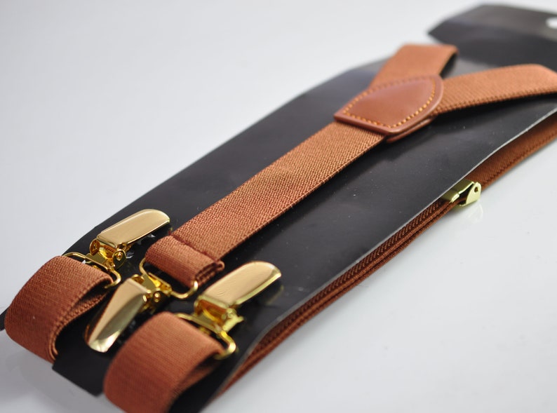 May include: Brown suspenders with gold metal clips. The suspenders are packaged on a black backing with a brown zipper.