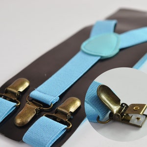 Puede incluir: Tirantes de color azul claro con clips de metal dorado antiguo. Los tirantes están hechos de un tejido suave y tejido y tienen un diseño sencillo.