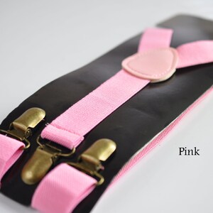 Peut inclure: Bretelles roses avec des clips dor&eacute;s et une sangle r&eacute;glable en cuir rose. Les bretelles sont sur un fond noir avec le mot "Rose" imprim&eacute; en bas &agrave; droite.