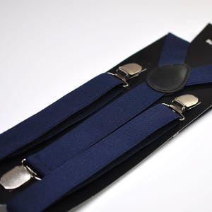 May include: A pair of navy blue suspenders with silver clips and a black leather patch that says "SUSPENDERS".