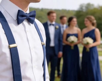 Może przedstawiać: Biała koszula z guzikami zestawiona z gładką granatową muszką i pasującymi granatowymi szelkami z metalowymi klipsami w kolorze złotym. Strój prezentuje formalną i schludną estetykę, podkreślając głęboki odcień niebieskiego materiału.