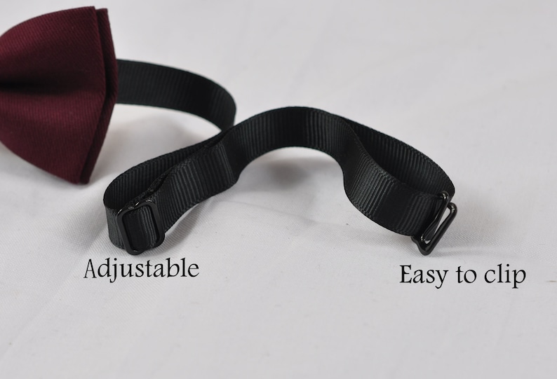 May include: A burgundy bow tie with a black adjustable strap and a metal clip. The text Adjustable is printed near the sliding buckle, and the text Easy to clip is printed near the metal hook fastener on the black fabric strap.