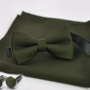 May include: A green bow tie, pocket square, and cufflinks set. The bow tie and pocket square are made of a textured fabric. The cufflinks are silver with a green fabric center.