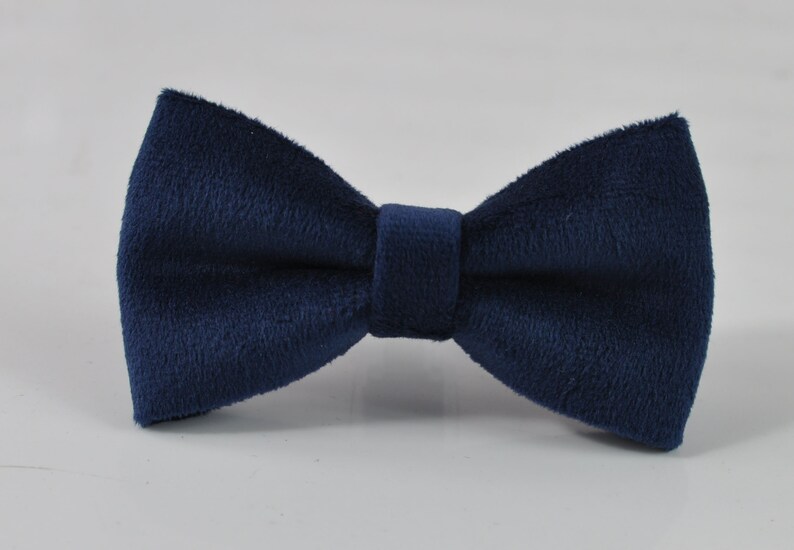 May include: A navy blue bow tie made of a soft, textured fabric. The bow tie is a classic accessory, perfect for formal events or adding a touch of sophistication to any outfit. The bow tie is centered on a white background.