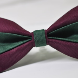 Könnte beinhalten: Eine burgunderrote und grüne Fliege. Die Fliege ist aus einem strukturierten Stoff gefertigt und hat ein schlichtes Design.