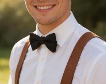 May include: A black bow tie is centered on a white collared shirt. Brown suspenders are visible on the shoulders. The image is a close-up of a person smiling.