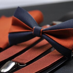 May include: A set of brown braces and a bow tie in a navy blue and brown colour scheme. The bow tie is made of fabric and has a classic design.