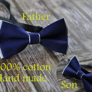 May include: Two navy blue bow ties with white trim. The larger bow tie is labeled "Father" and the smaller bow tie is labeled "Son". The text "100% cotton Hand made" is also visible.