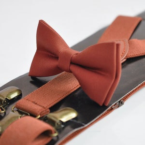 May include: A set of brown suspenders and a matching brown bow tie. The suspenders have metal clips and the bow tie is made of a soft fabric.