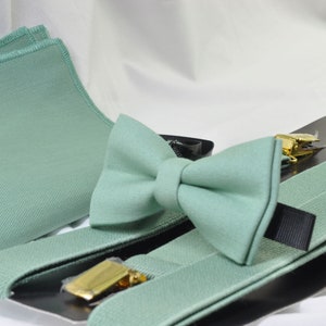 May include: A set of mint green suspenders, bow tie, and pocket square. The suspenders have black elastic straps and gold-tone clips. The bow tie is made of a soft fabric and has a classic shape. The pocket square is a small square of fabric that can be folded and placed in a jacket pocket.