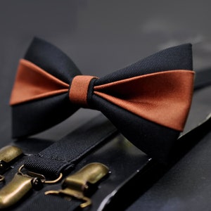May include: A black and brown bow tie with suspenders. The bow tie has a brown stripe across the middle. The suspenders are black with gold metal clips.
