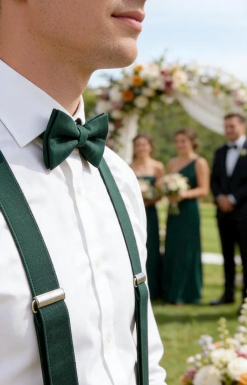 May include: A crisp white button-down shirt paired with a solid dark forest green bow tie and matching dark forest green braces. The braces feature polished silver-toned metal clips that securely fasten to the fabric of the shirt.