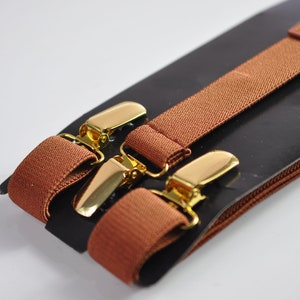 May include: Brown suspenders with gold metal clips. The suspenders are packaged on a black card with a brown leather trim.
