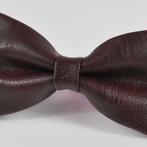 May include: A brown faux leather bow tie. The bow tie is made of a textured material and has a classic shape.