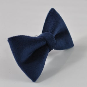 May include: A navy blue bow tie made of a soft, textured fabric. The bow tie is knotted in the center and has a classic butterfly shape. The accessory is set against a white background.