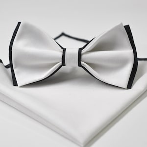 Puede incluir: Pajarita blanca con ribete negro y un pañuelo de bolsillo blanco con ribete negro.